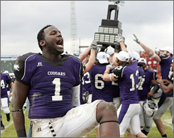 Sioux Falls linebacker Marlon Lobban celebrates as teammates hoist the NAIA trophy in the background after the Cougars defeated Lindenwood to win the championship.
