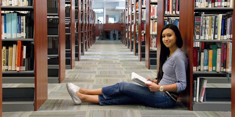 Girl sitting on floor of library with back up against book case